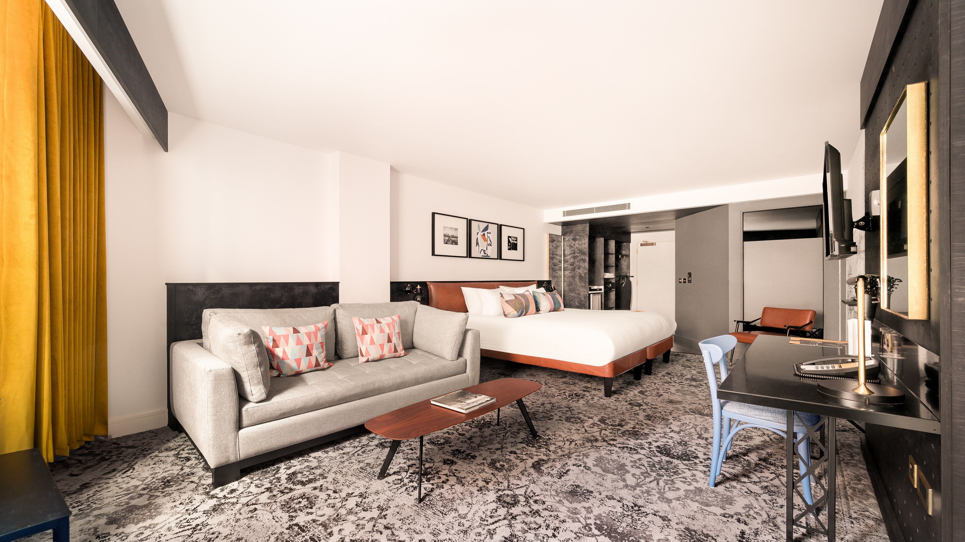 A modern hotel room with a sofa, a bed, a desk, and a chair.