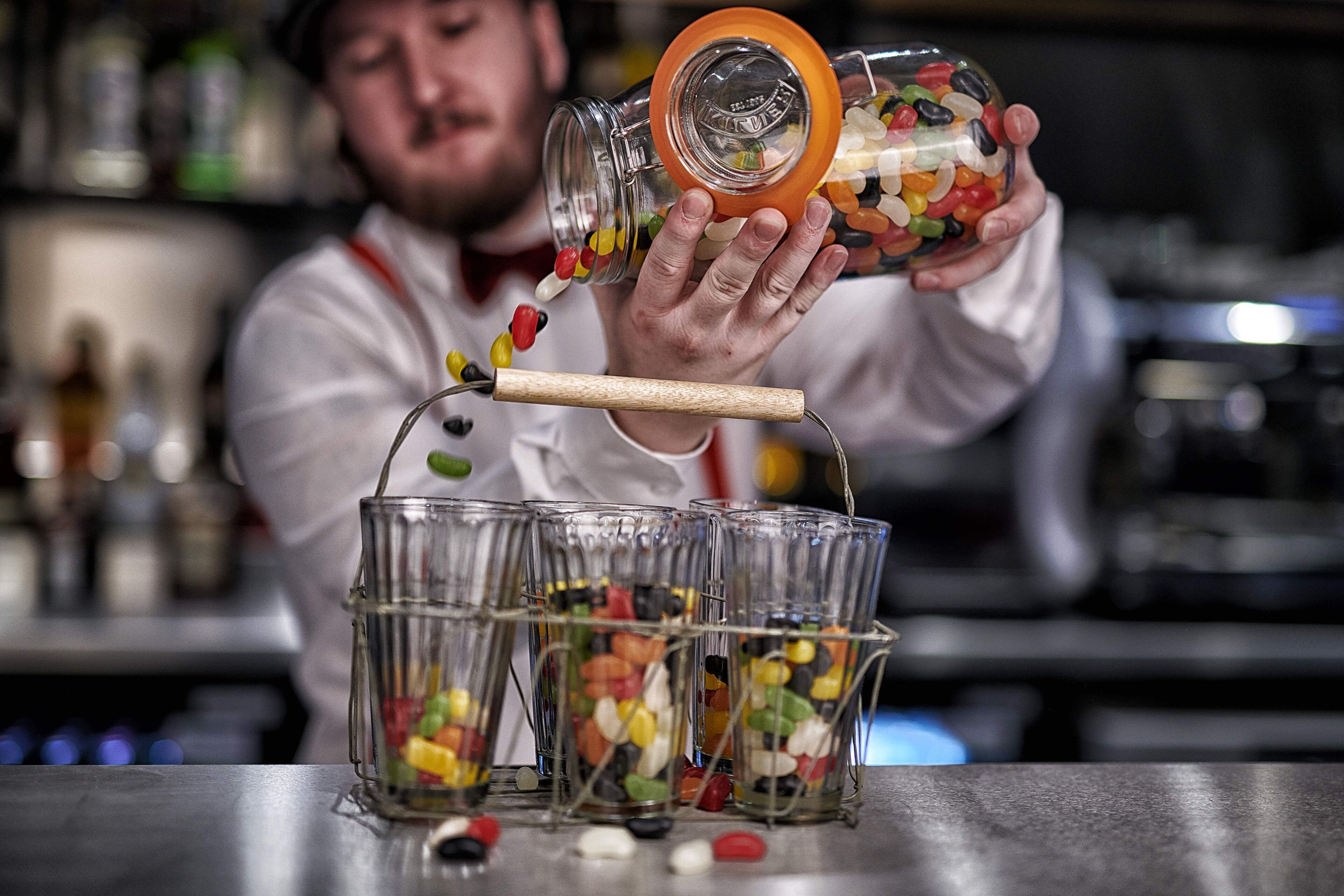 A person pouring colorful candies into a glass container.