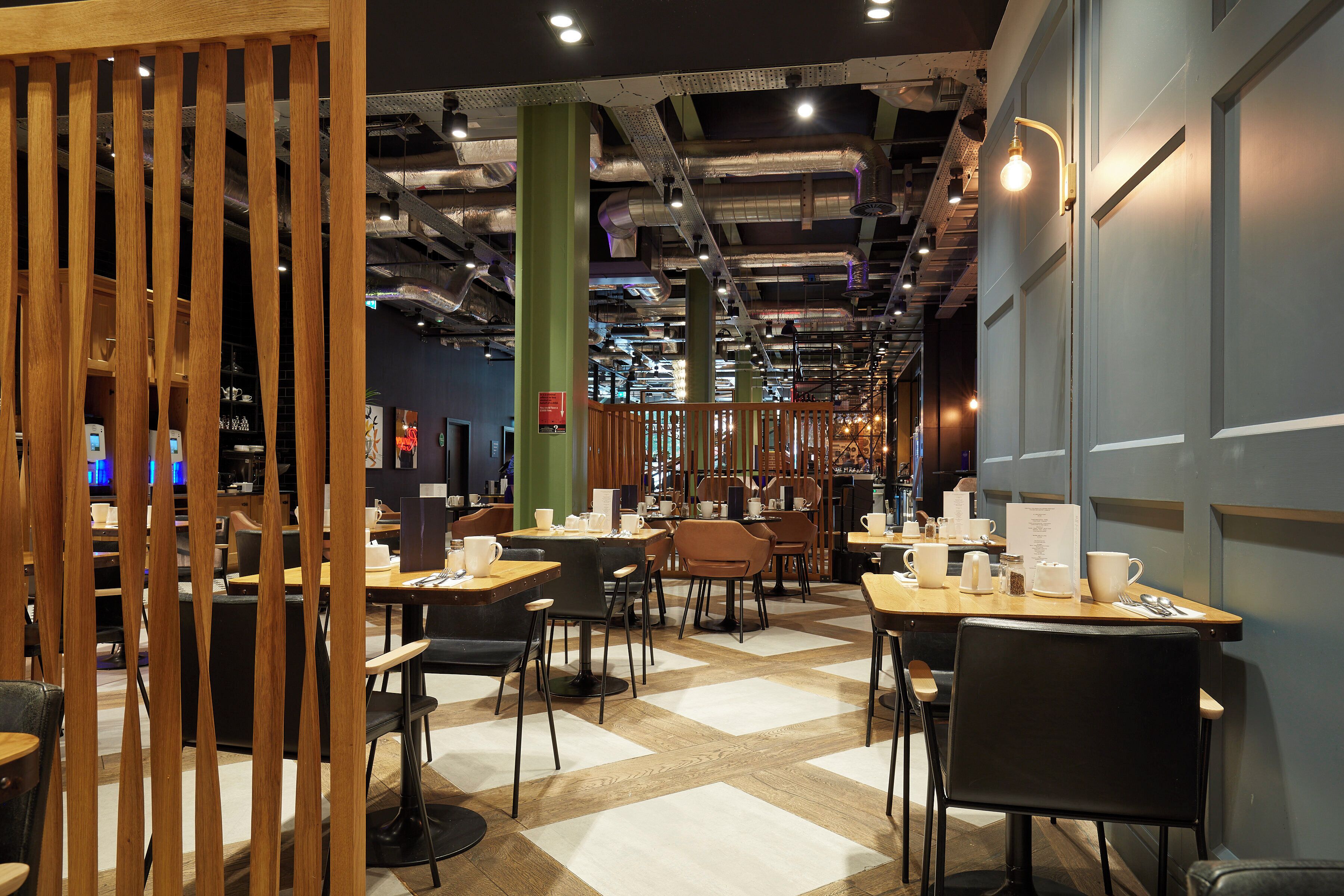 Un café moderne avec des cloisons en bois, un sol à carreaux et différents types de sièges, notamment des tables et des chaises.