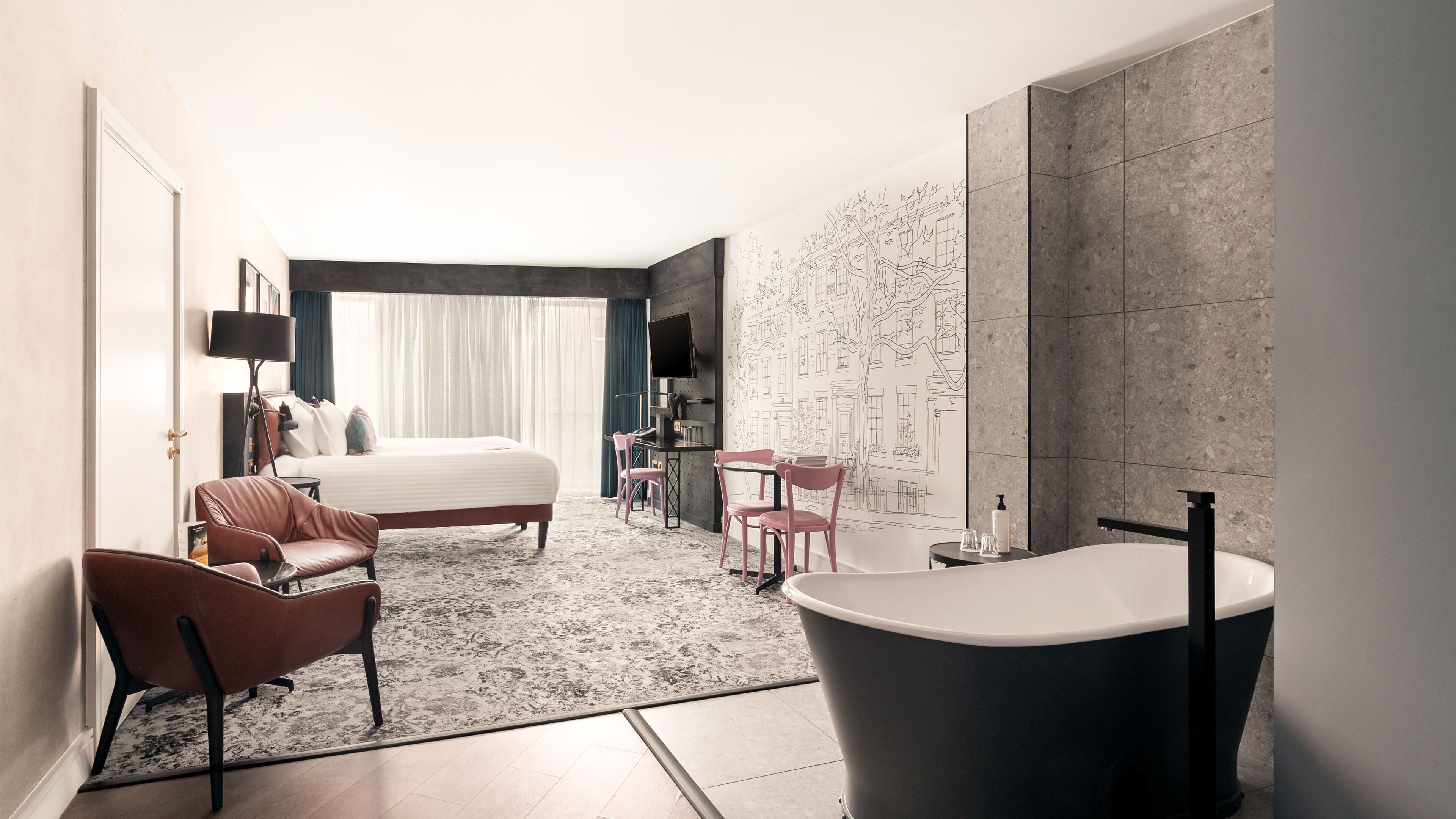 A modern hotel room with a large bed, a sitting area with chairs, a desk, a flat-screen TV, and a large bathtub.