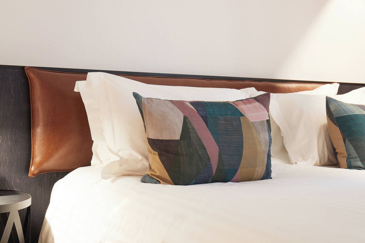 A bed with a brown headboard, multiple pillows, and a round side table.