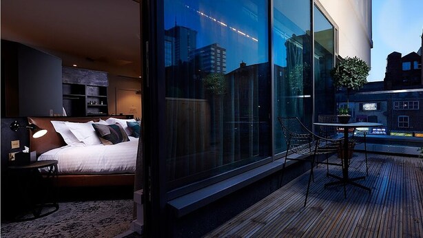 A modern bedroom with a large bed, bedside tables, and a view of the city through floor-to-ceiling windows. - voco Manchester City Centre by IHG (Manchester)