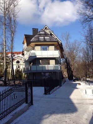 A multi-story building with a balcony, a gated entrance, and a snow-covered ground.