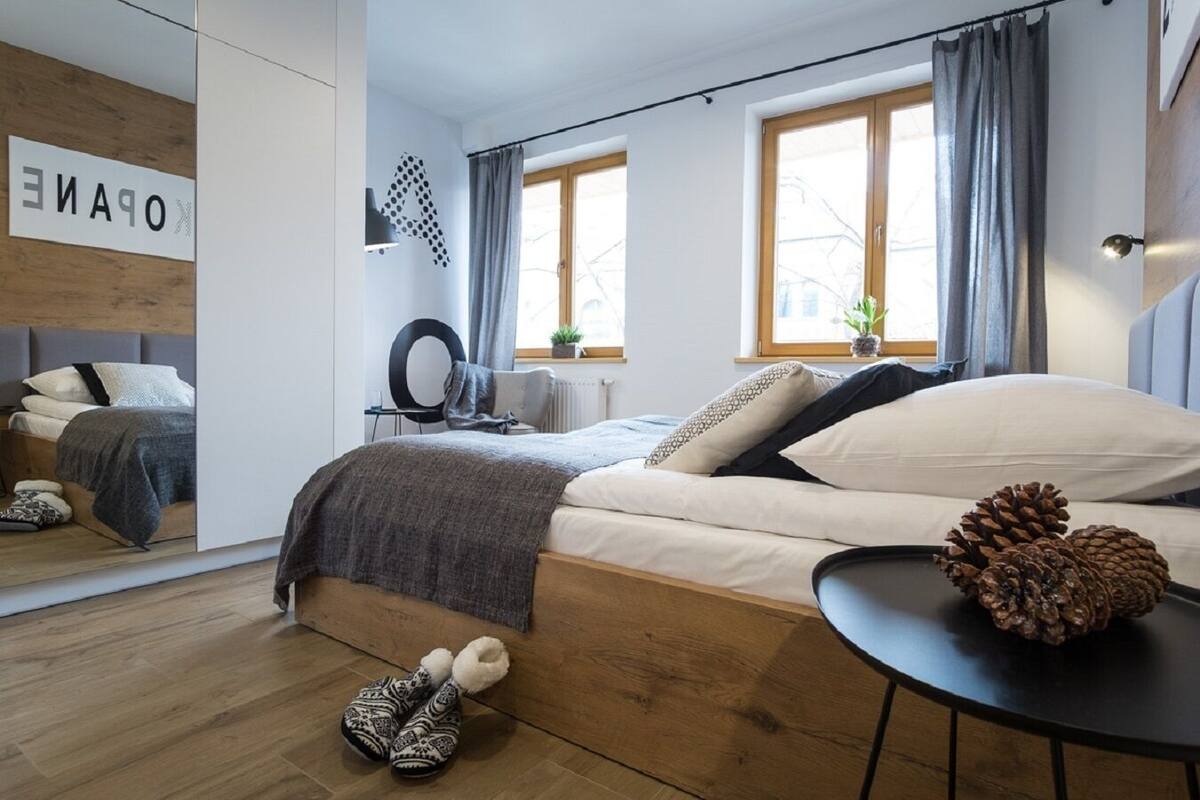 A modern bedroom with a wooden bed, a small round table, a mirror, and a view of the outside.
