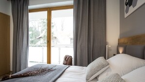 Et hotelværelse med en seng, grå gardiner, udsigt til det fri og en træsenggavl.