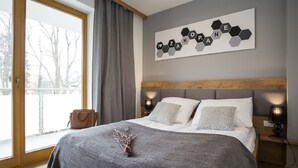 Et moderne soveværelse med en stor seng, gråt sengetøj, en træsenggavl og et kunstværk på væggen.