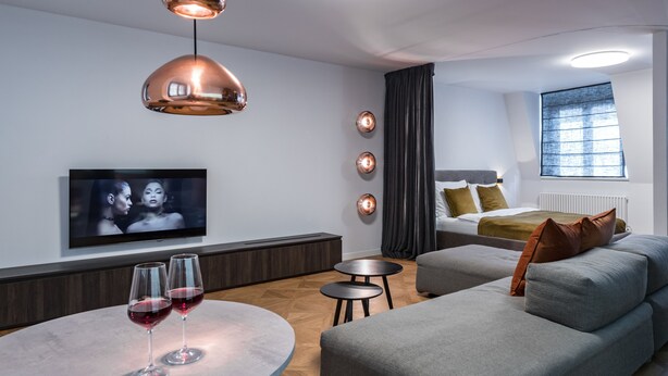 A modern living room with a sofa, a coffee table, and a TV mounted on the wall. There are two pendant lights hanging above the table. - Exclusive home in heart of Prague (Prague)