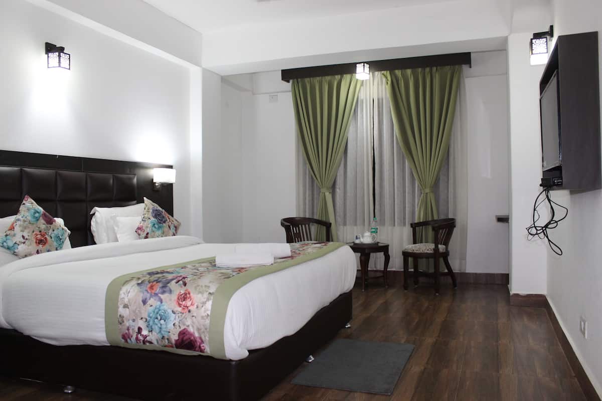 A hotel room with a large bed, a small table with chairs, a TV mounted on the wall, and a window with curtains.