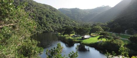 A serene landscape with a river, lush greenery, and a small building near the water.