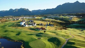 An aerial view of a golf course with houses and a mountain range in the background. - Aleph Cottage George (George)