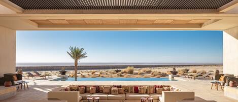 Un espacio lounge al aire libre con piscina, asientos y vistas al desierto.