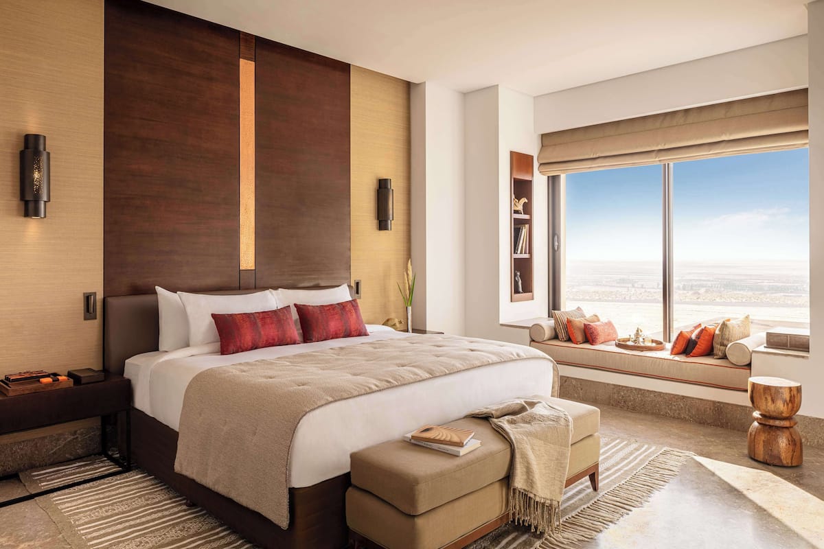 A modern hotel room with a large bed, a seating area by the window, and a view of the cityscape.