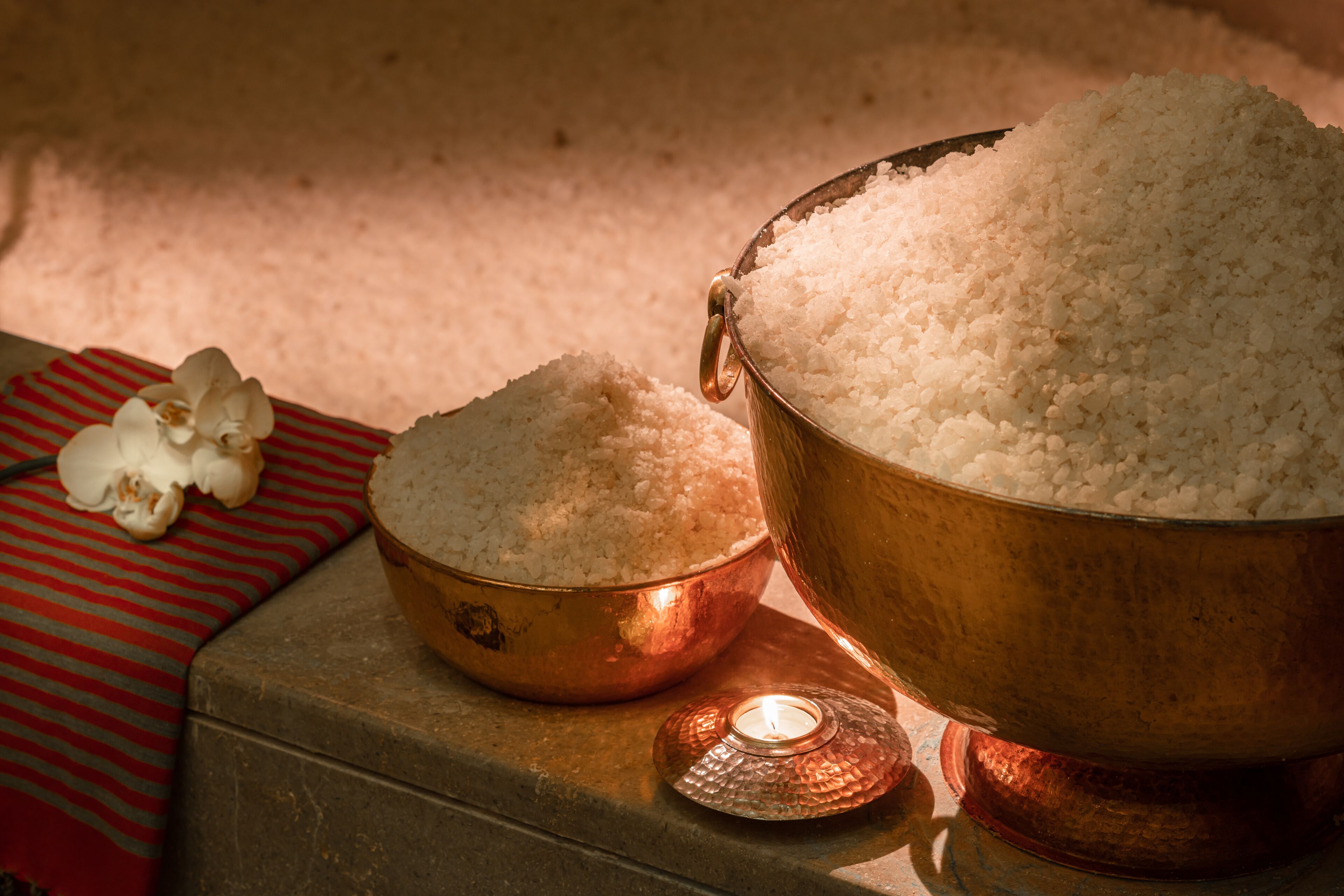 Un bol en cuivre rempli de riz blanc, un plus petit bol contenant également du riz, et une bougie allumée sur une table.