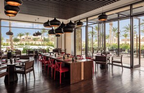 Um restaurante moderno com uma ilha central, cadeiras vermelhas e luminárias pendentes.