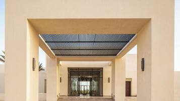 A modern building entrance with a covered walkway, palm trees, and a clear sky.