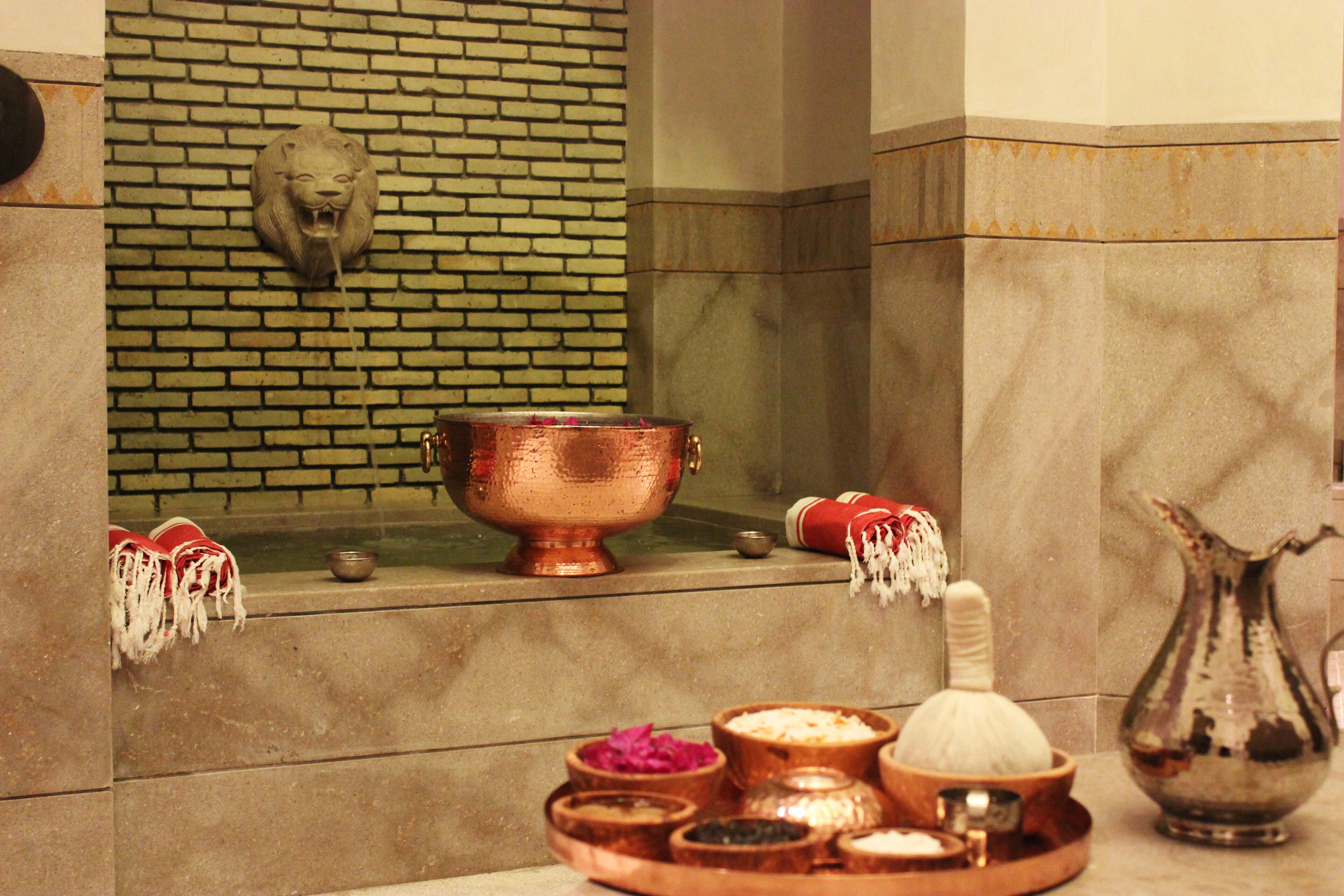 A room with a brick wall, a lion head decoration, a copper bowl, and various small containers.