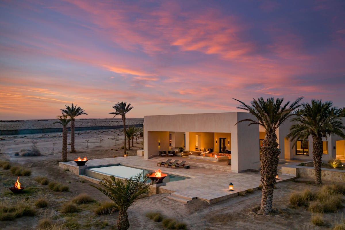 A modern resort with a pool, outdoor seating, and palm trees.