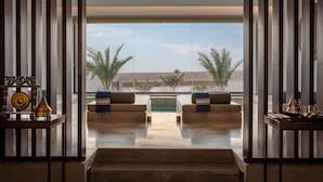 A modern interior with a view of palm trees and a pool. There are two sofas with cushions and a small table with decorative items. - The Mora Sahara Tozeur (Tozeur)