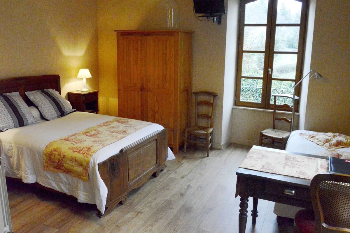 A bedroom with a bed, a desk, a chair, a wardrobe, a window, and a lamp.
