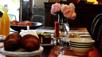 A dining table with a basket of croissants, a bowl of fruit, a vase with flowers, and a bottle of orange juice.