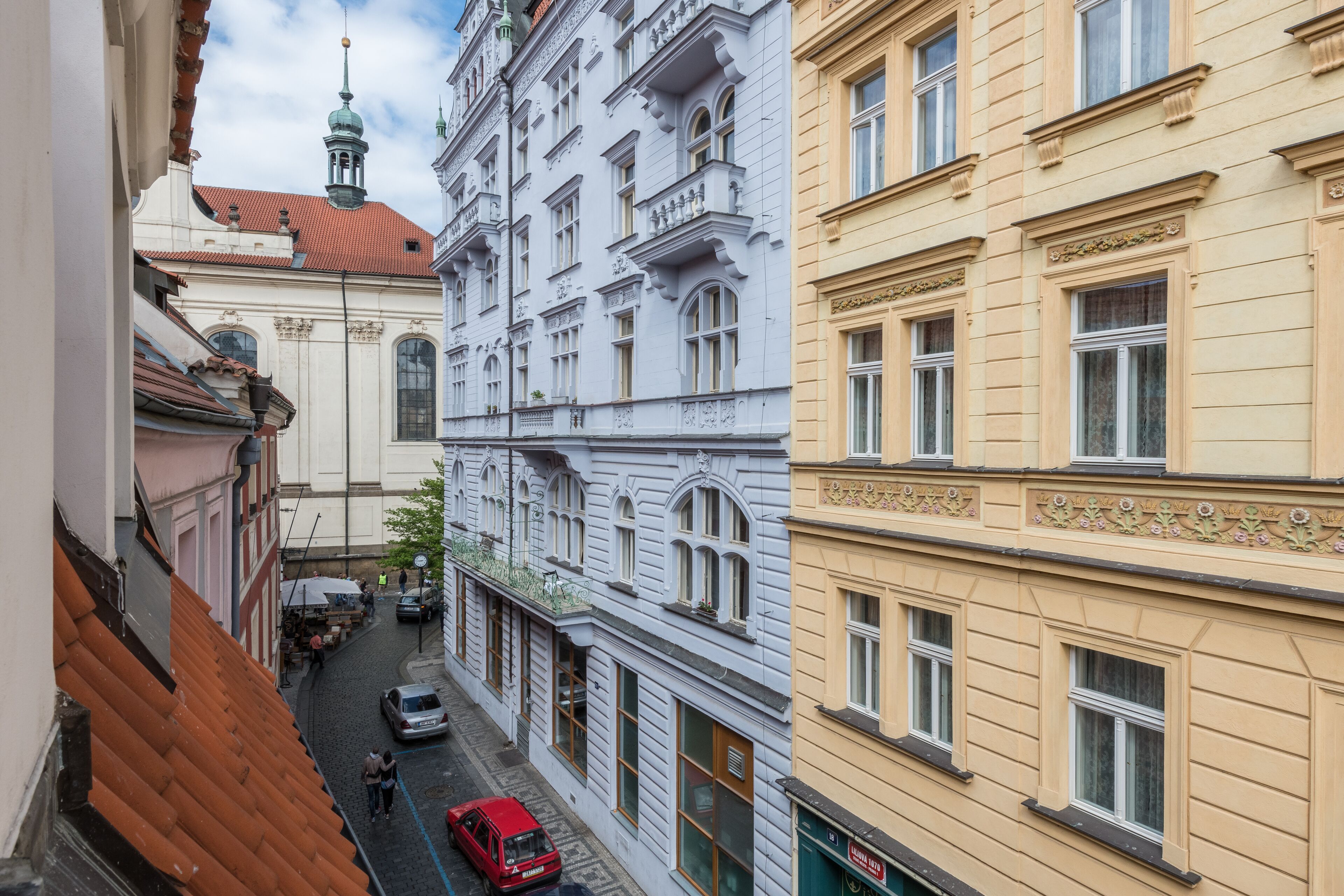 A narrow street with buildings on either side, featuring classic architecture with ornate details and large windows.