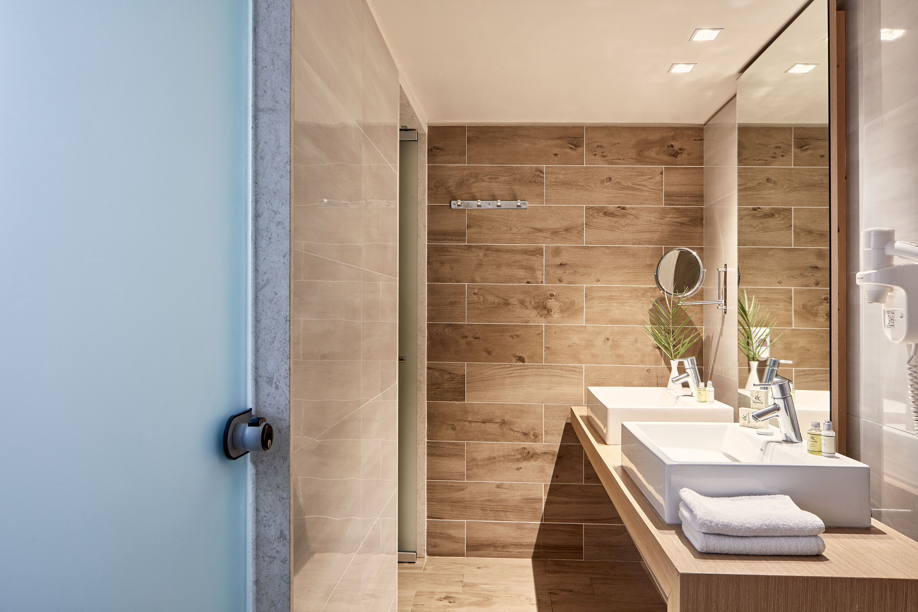 Un baño moderno con un espejo grande, dos lavamanos y zona de ducha.
