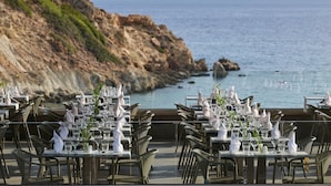 Un restaurante con mesas dispuestas para comer, con vista a una costa rocosa y al mar.