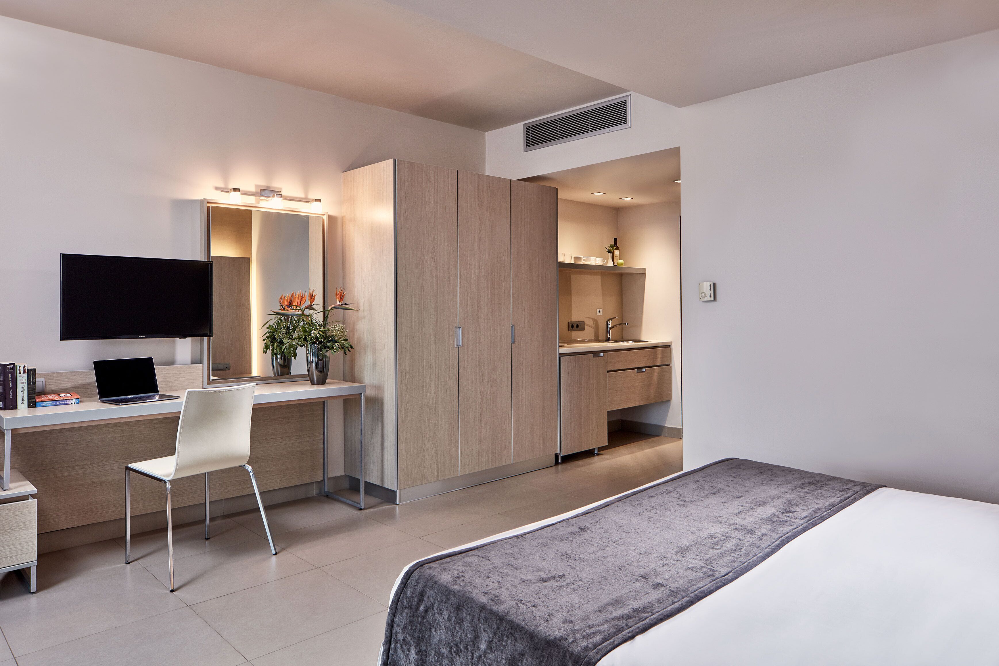 Une chambre d’hôtel moderne équipée d’un lit, d’un bureau avec une chaise, d’une télévision et d’une kitchenette.