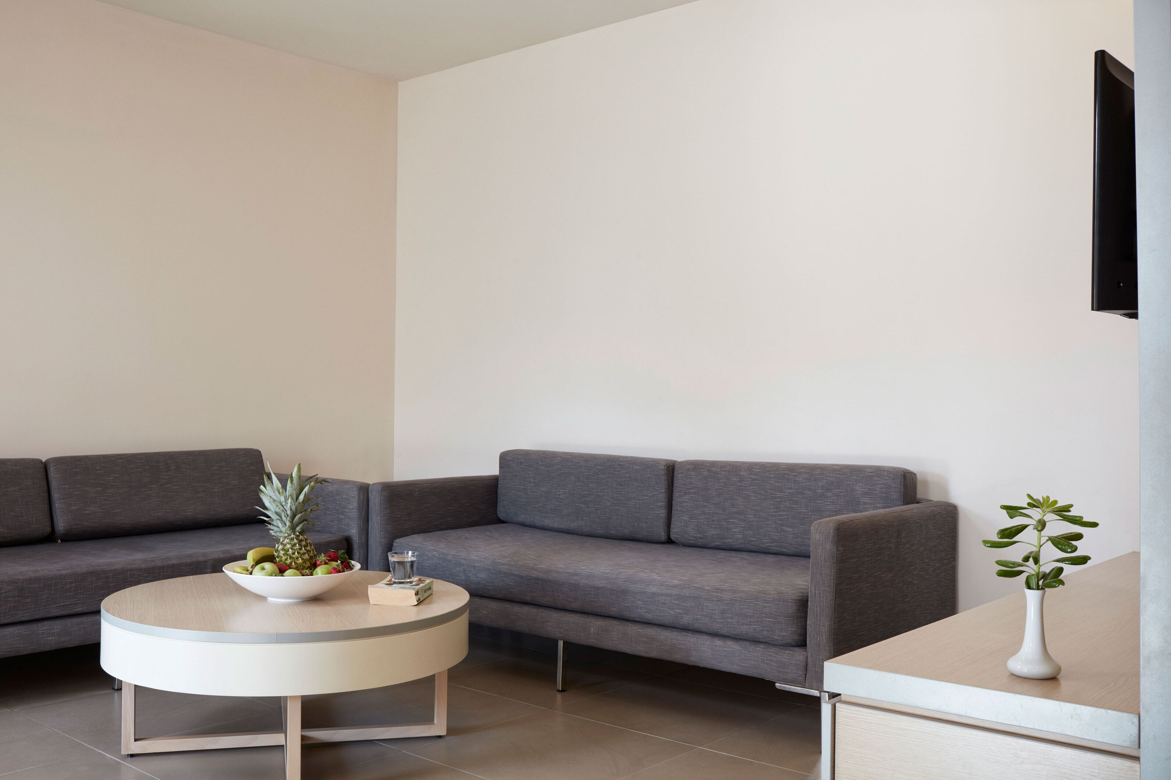 A modern living room with a grey sofa, a round coffee table with a fruit bowl, and a small white vase on a side table.