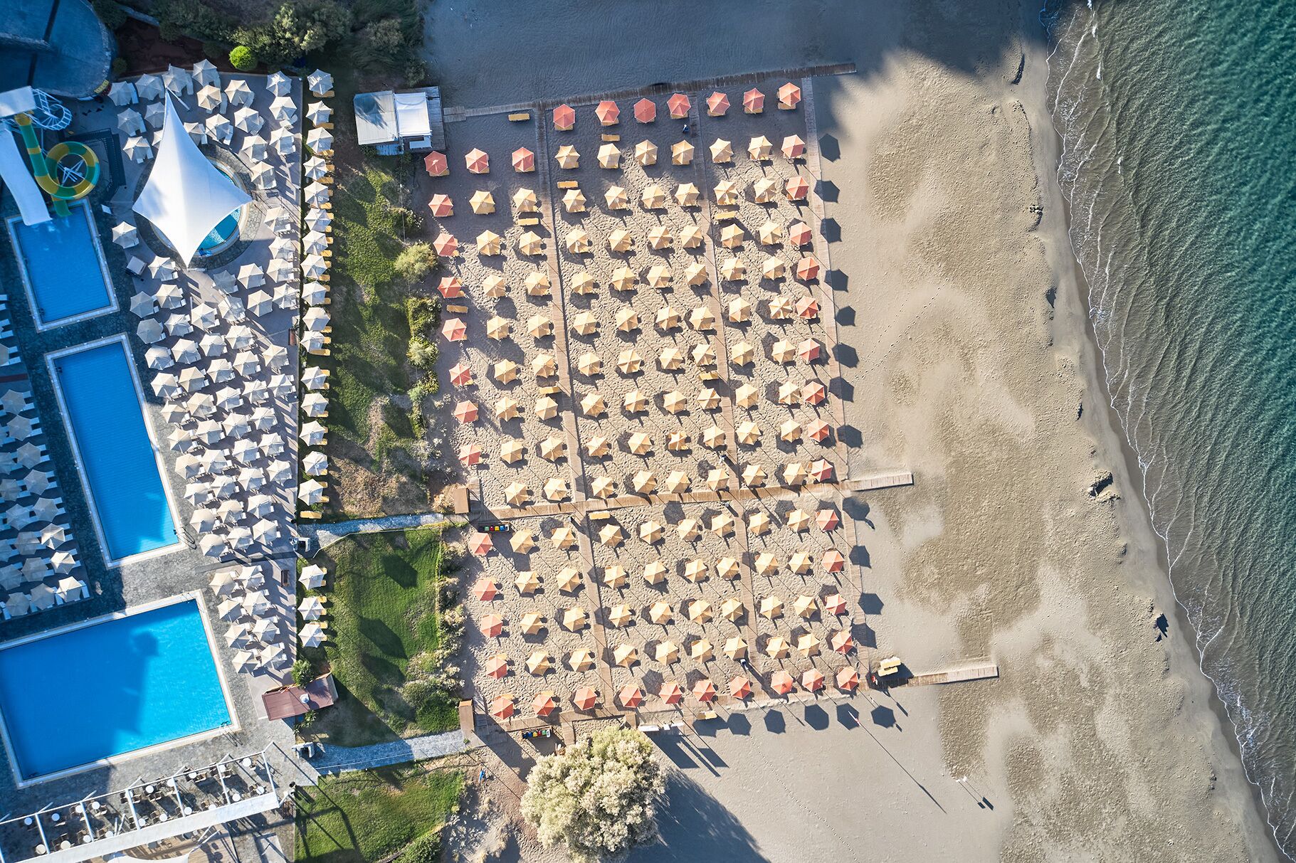 An aerial view of a beach with numerous umbrellas and a swimming pool.