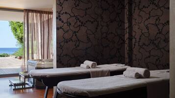 Ein Spa-Behandlungsraum mit zwei Massageliegen, Blick auf das Meer und einer Wand mit Muster.