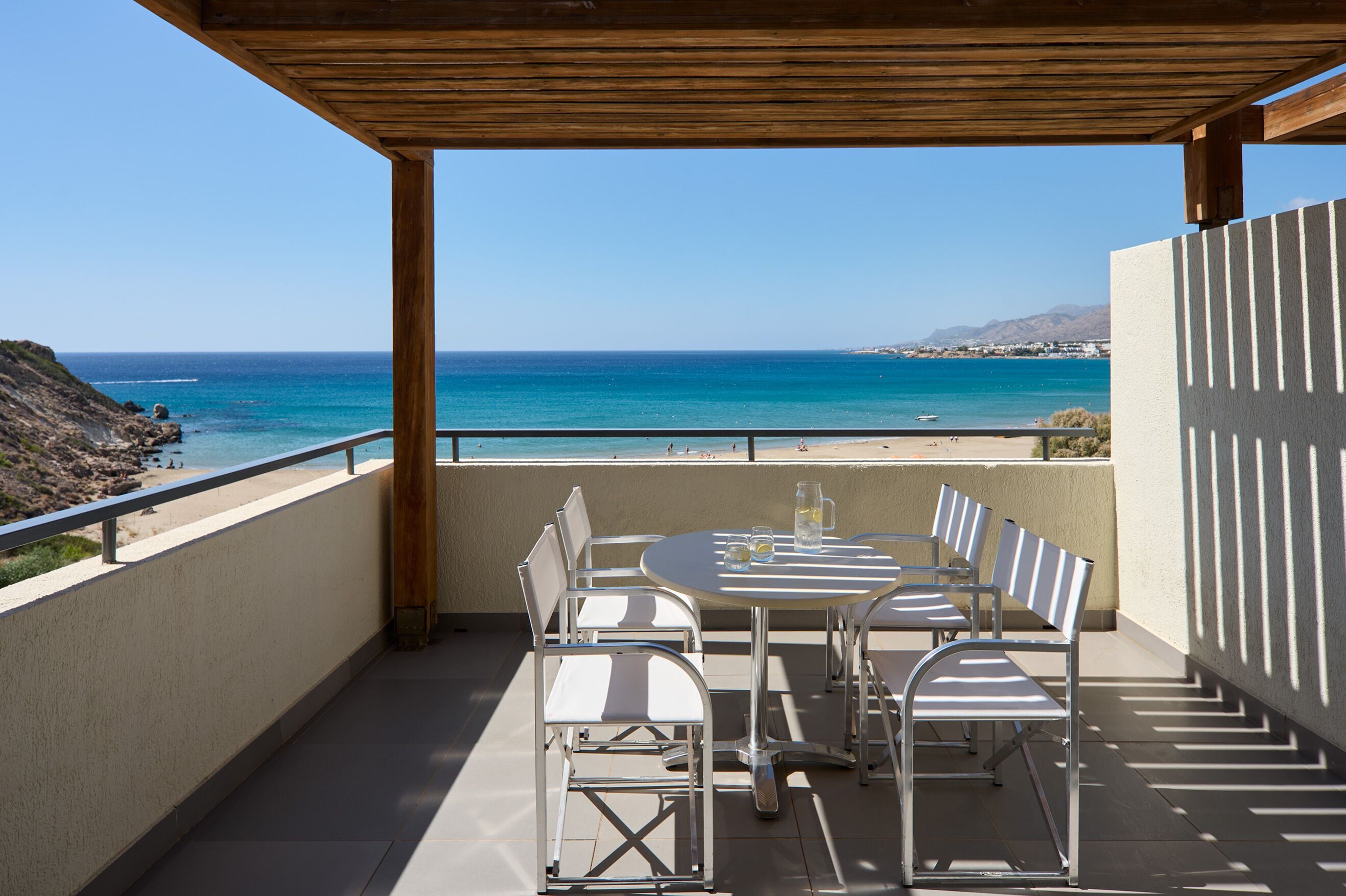 A covered outdoor seating area with a table and chairs, overlooking a beach and ocean.