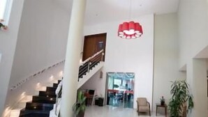 Un intérieur spacieux avec un escalier, une grande plante et un luminaire suspendu rouge.