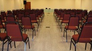Une salle de conférence avec des rangées de chaises rouges, un pupitre et un écran de projection.
