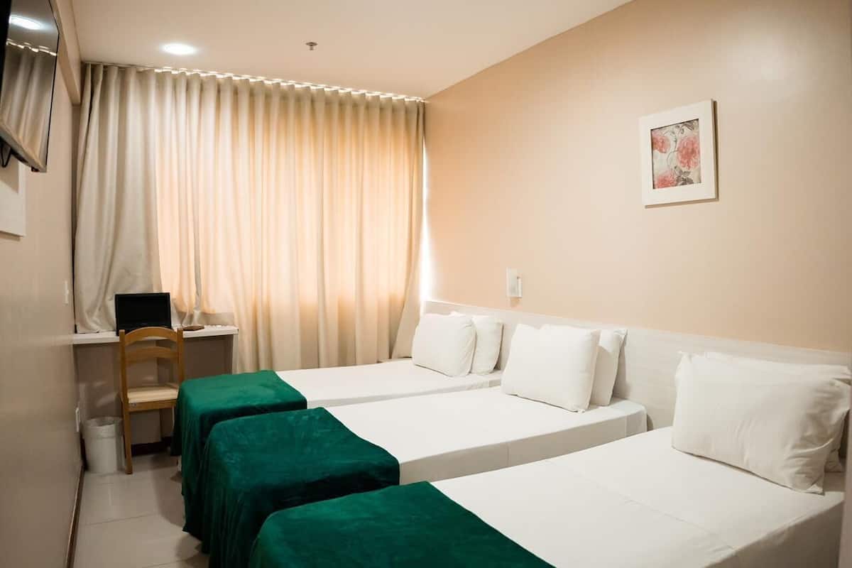 A hotel room with two single beds, a desk with a chair, a computer, and a window with curtains.