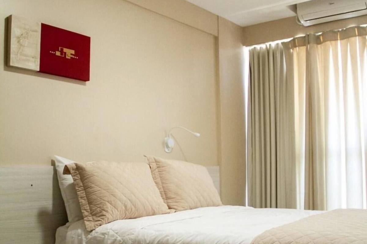 A hotel room with a bed, a wall-mounted air conditioner, and a window with curtains.