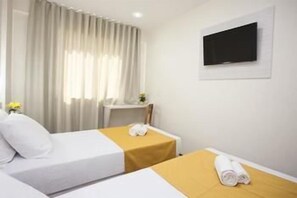 A hotel room with two beds, a TV on the wall, and a window with curtains. - Green Hoteis (CABO FRIO)