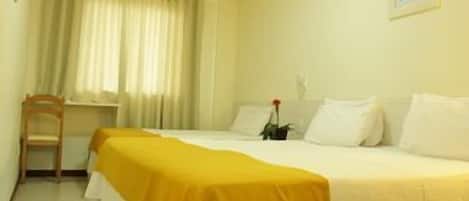 Une chambre d’hôtel avec un lit, une chaise, un bureau et une fenêtre avec des rideaux.