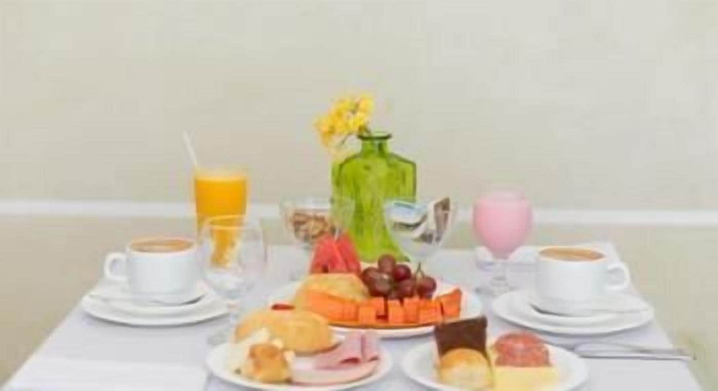 Uma mesa de café da manhã com pratos de comida, um vaso com flores e xícaras de café.