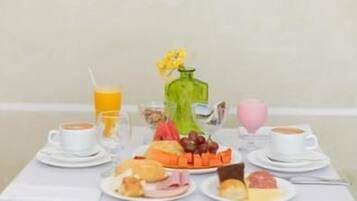 Uma mesa de café da manhã com pratos de comida, um vaso com flores e xícaras de café.