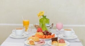 A breakfast table with plates of food, a vase with flowers, and cups of coffee. - Green Hoteis (CABO FRIO)