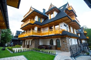 A multi-story house with wooden balconies, stone walls, and a well-maintained garden. - Apart-Center Zakopianskie Tarasy Spa (Zakopane)