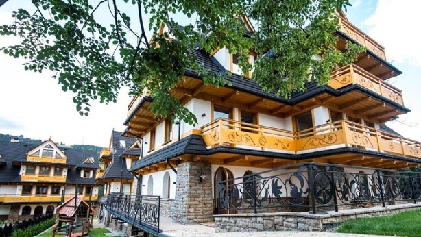 A traditional chalet-style building with multiple balconies, stone foundations, and a well-maintained lawn.