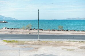 A coastal road with a lighthouse in the distance, rocky shoreline, and sparse vegetation. - Angela & Thalia Apartments (Kos)