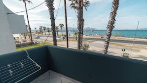 A balcony with a view of a coastal road, palm trees, and a body of water. - Angela & Thalia Apartments (Kos)