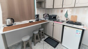 A compact kitchen with a coffee maker, kettle, and a small refrigerator. There are two stools and a sink. - Angela & Thalia Apartments (Kos)