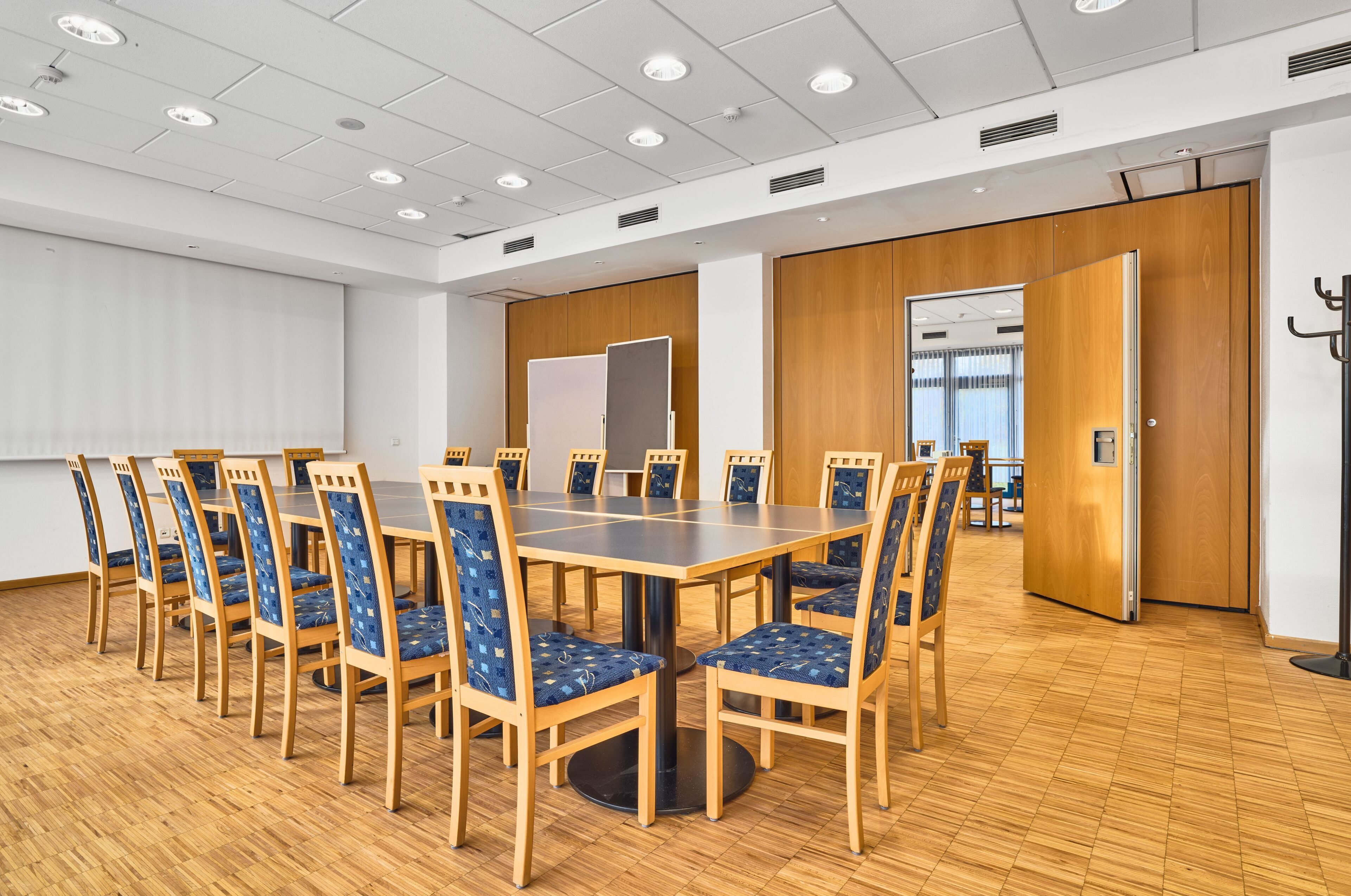 A conference room with a large table and chairs, wooden flooring, white walls, and a door leading to another room.