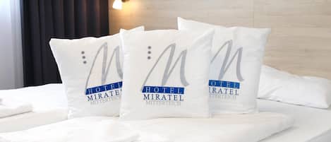 Una cama de hotel con tres almohadas que muestran el logotipo y el nombre del hotel.