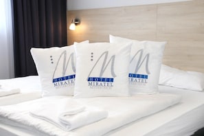 Una cama de hotel con tres almohadas que muestran el logotipo y el nombre del hotel.
