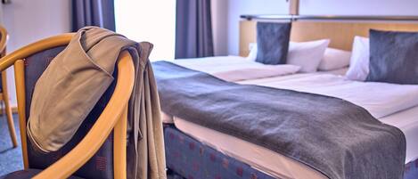 A hotel room with a bed, a chair with a jacket on it, and a wall-mounted lamp.
